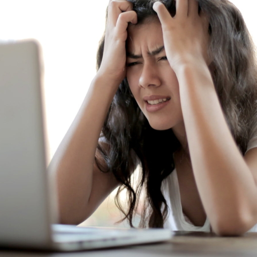 Mulher com as mãos na cabeça e expressão de frustração em frente ao notebook