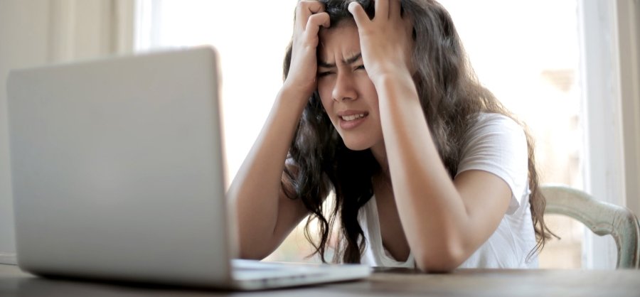 Mulher com as mãos na cabeça e expressão de frustração em frente ao notebook