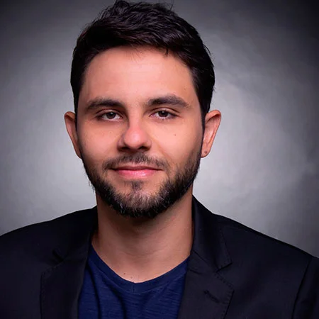 Retrato de um homem de cabelos escuros, barba baixa, usando roupa preta,.