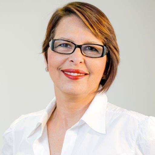 Sobre Sites&Cia 17 Foto de uma mulher com óculos de aros pretos, cabelos curtos avermelhados, sorrindo, de blusa branca.