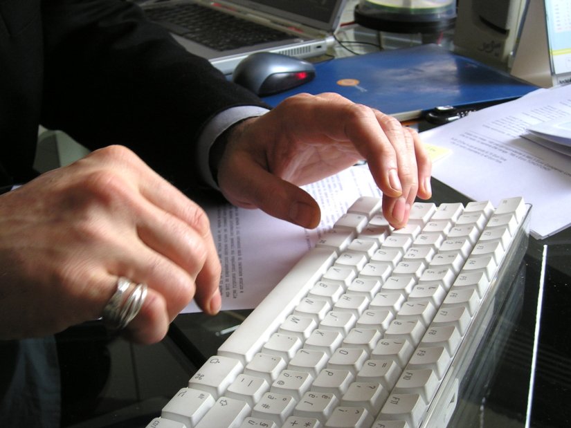 Teclado branco em uma mesa de papeis sendo usados por um par de mãos aparentemente masculinas