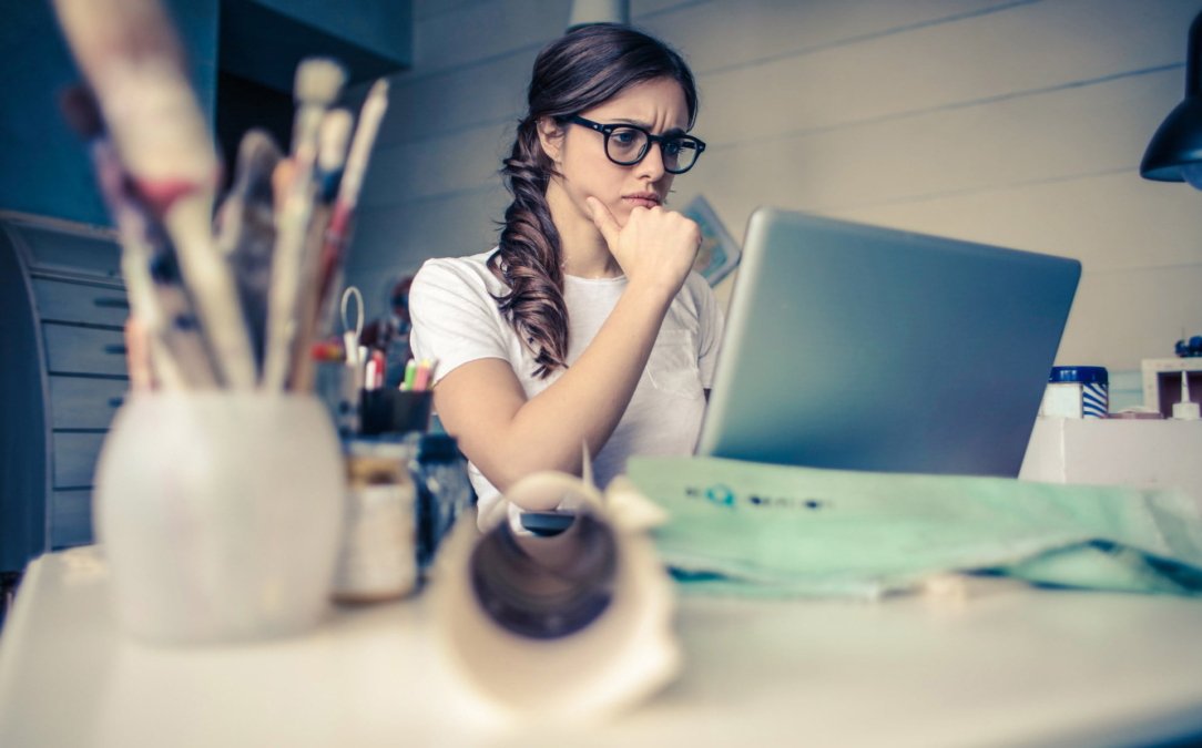 Mulher de cabelos compridos e óculos com a mão no queixo usando um notebook
