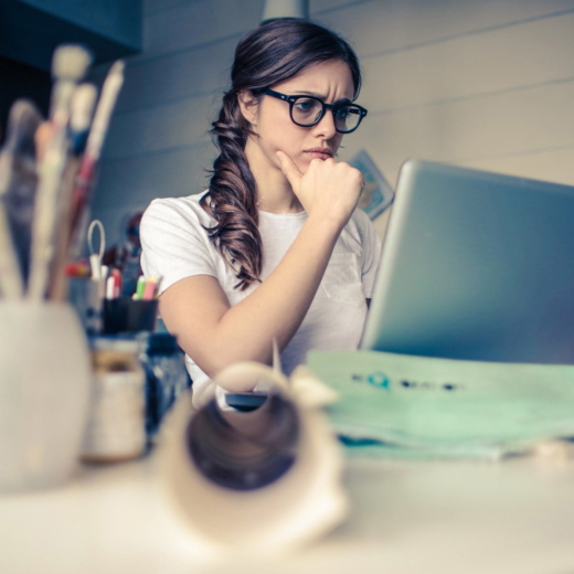 Mulher de cabelos compridos e óculos com a mão no queixo usando um notebook